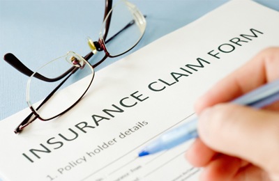 An insurance claim form with a hand holding a pen and a pair of glasses