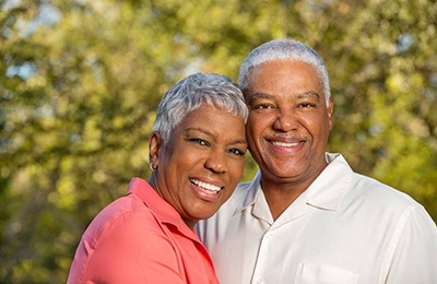 Older couple with dental implants in Brownstown smiling outside