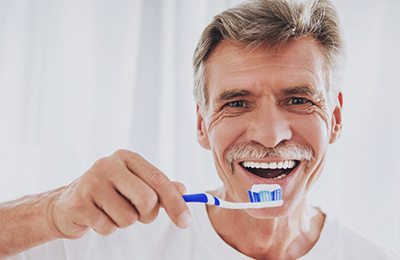 older man in white t-shirt brushing his teeth 